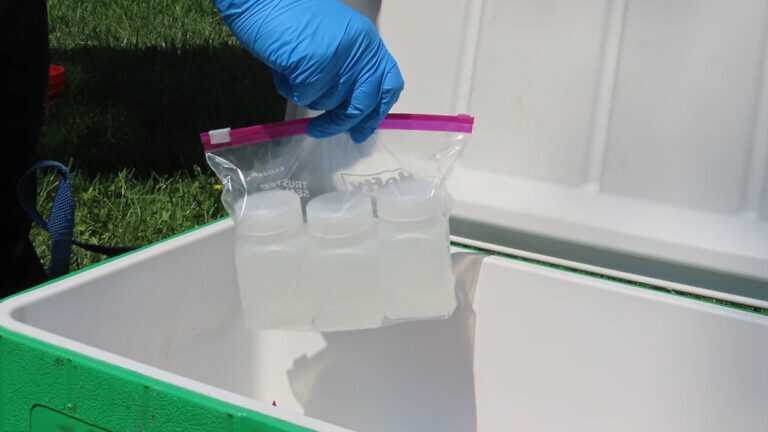 A worker wearing PPE placing three water samples inside a container