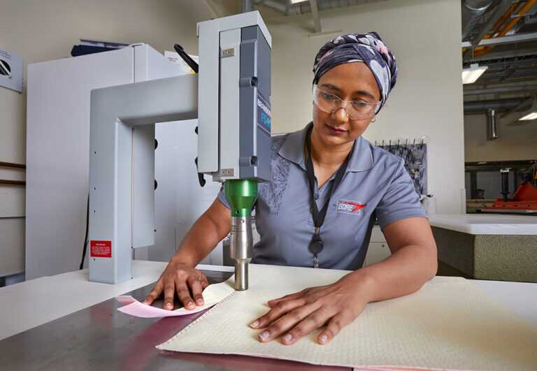 Woman wearing protective gear and a Gore uniform using a specialized device to cut a material