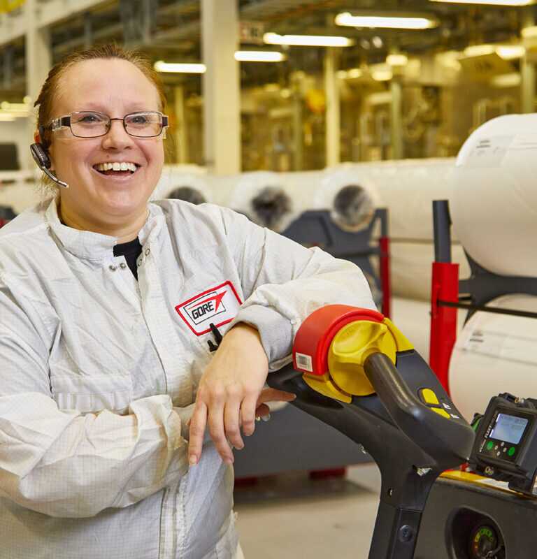 A woman wearing a Gore uniform smiling in towards the camera while leaning on a stalled motorized dolly