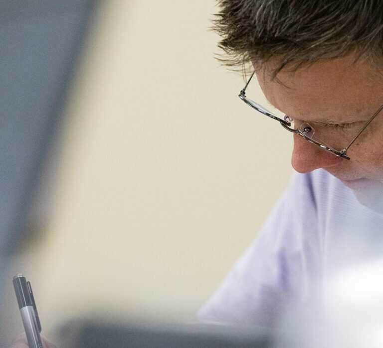 A close up of a mans face wearing glasses in the middle of writing a report
