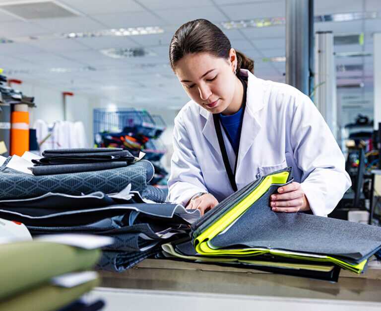 A woman wearing a lab coat examining a stack of various materials