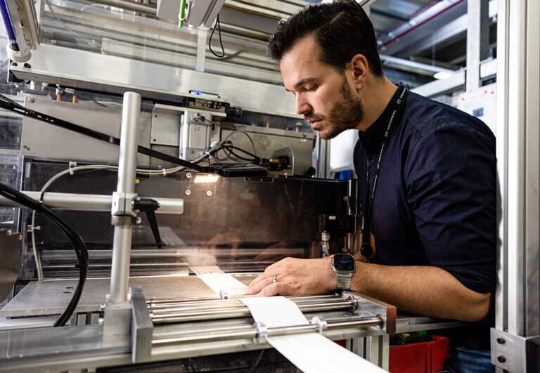A man running a long strip of material through a specialized machine
